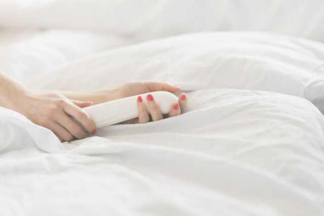 Hand of woman holding sex toy in bed