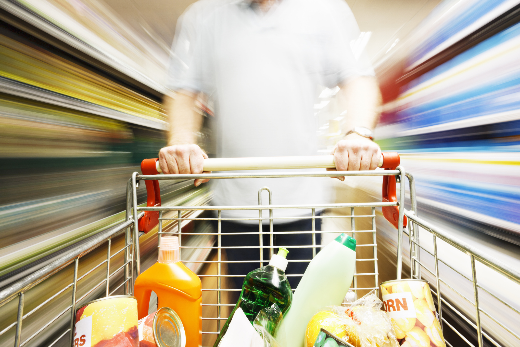 Speed blurs male shopper in supermarket with full shopping cart