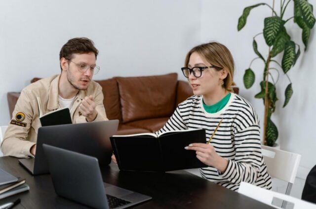 A man and a woman discussing something while showing each other notes.